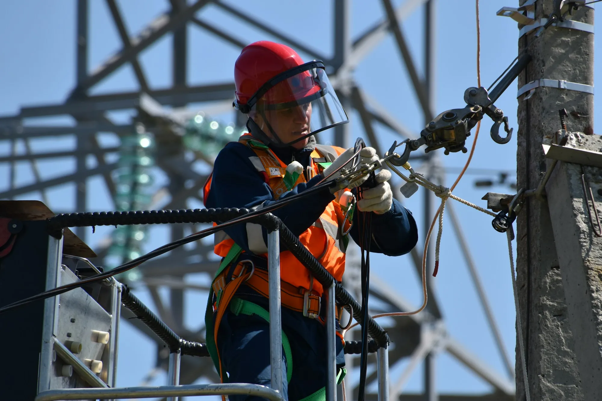 Lineman in a red helmet with a face shield working on high-voltage equipment