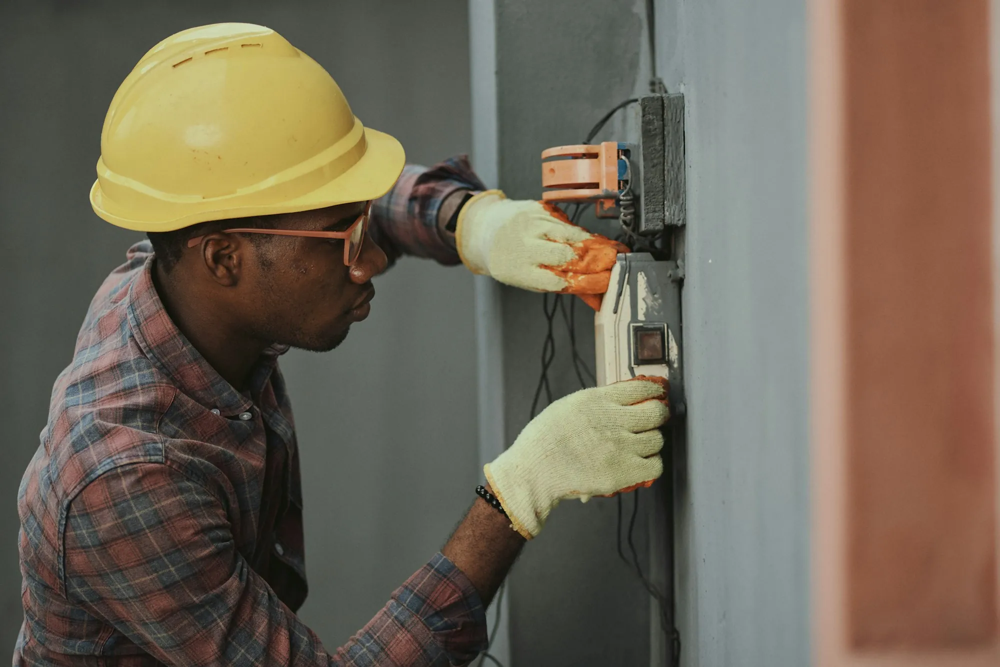 Tradesman in a yellow helmet and plaid shirt adjusting an exterior meter base